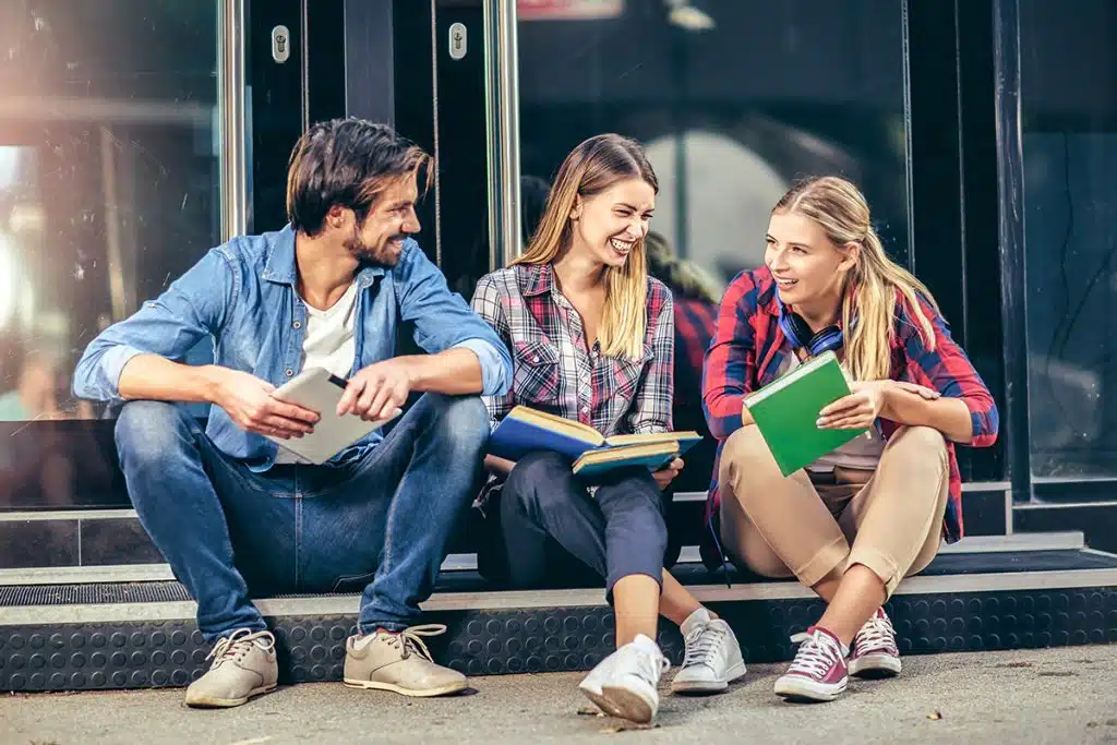 A group of college students talk outside of a building.